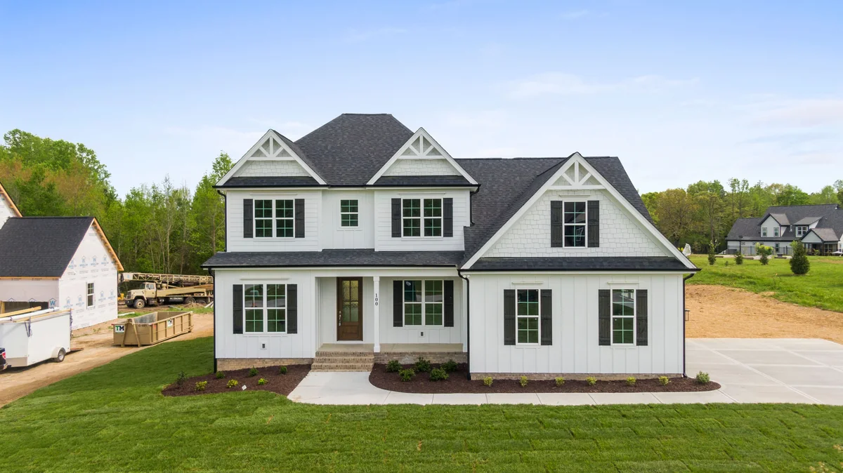 White two-story home with black shutters, a pitched roof, and a lawn.