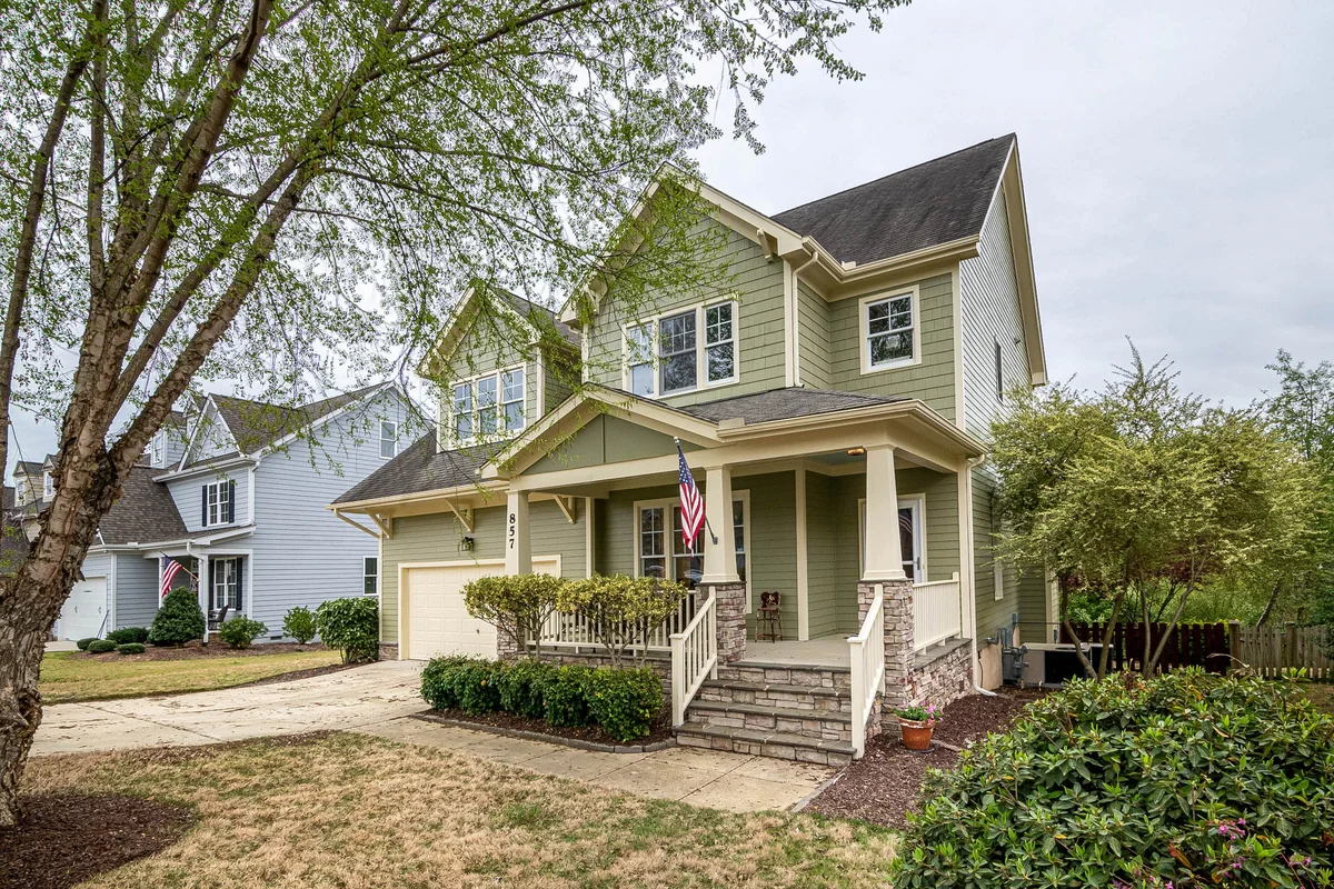 Olive-colored clapboard home with a covered front porch and mature trees.