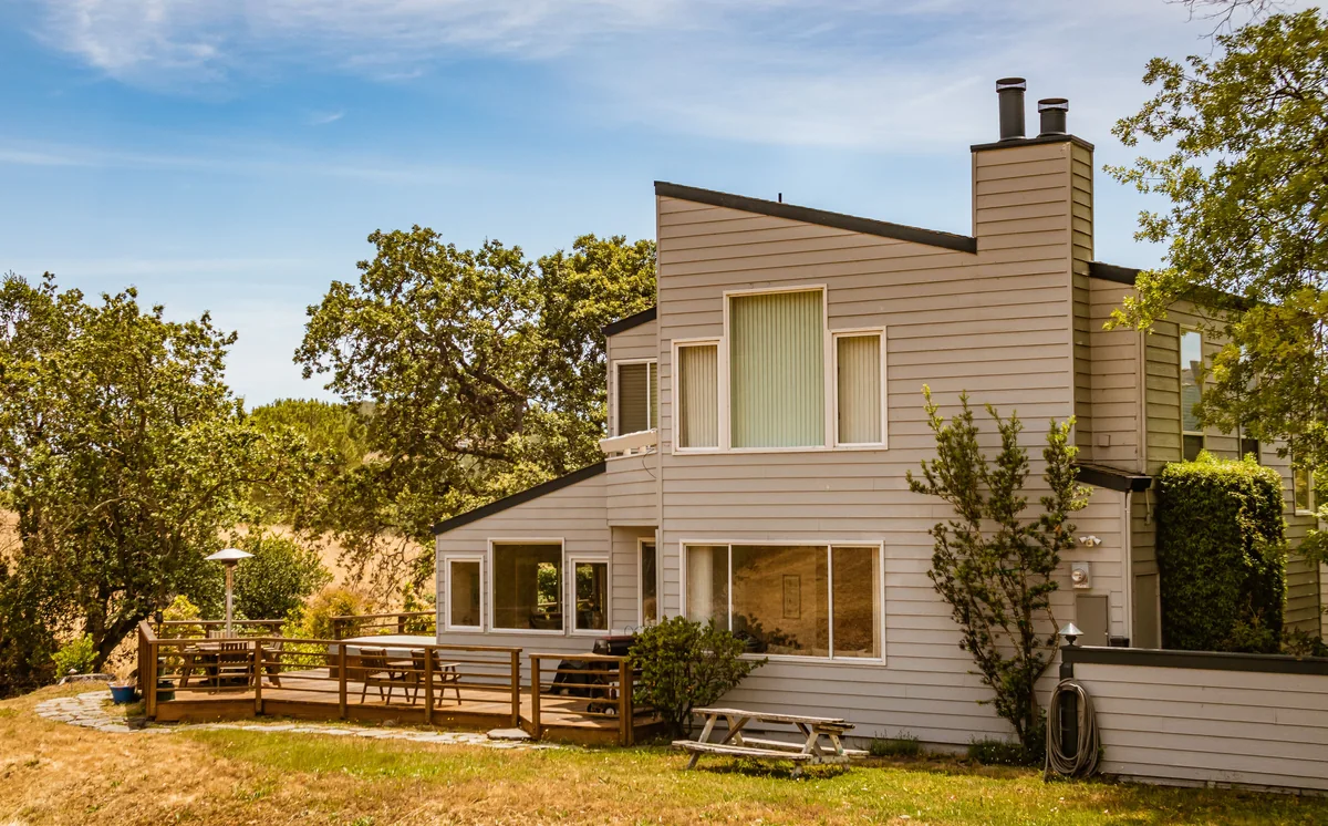 Contemporary wood-sided house with a broad backyard and mature trees.