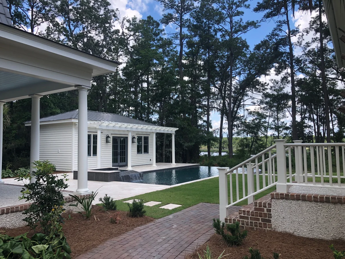 White house with a shaded porch beside a swimming pool.