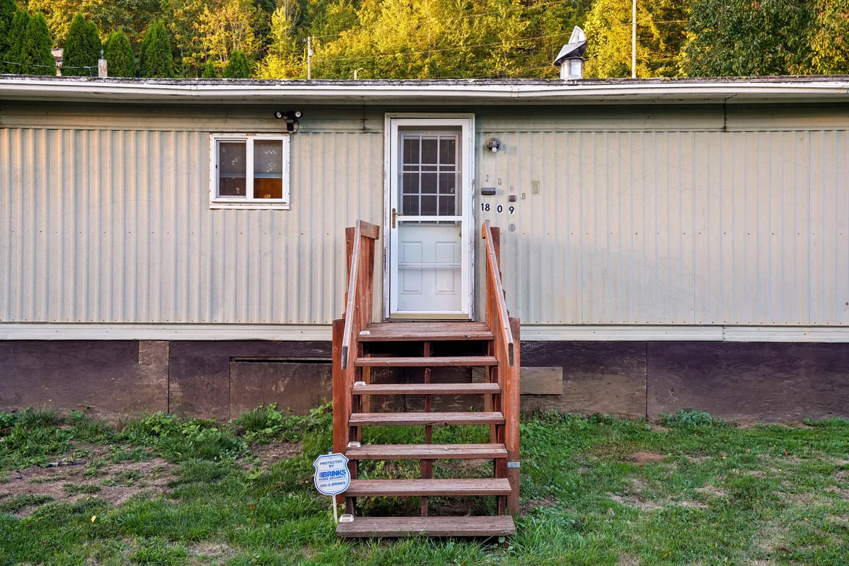 Single-story mobile home with light siding and wooden front steps.