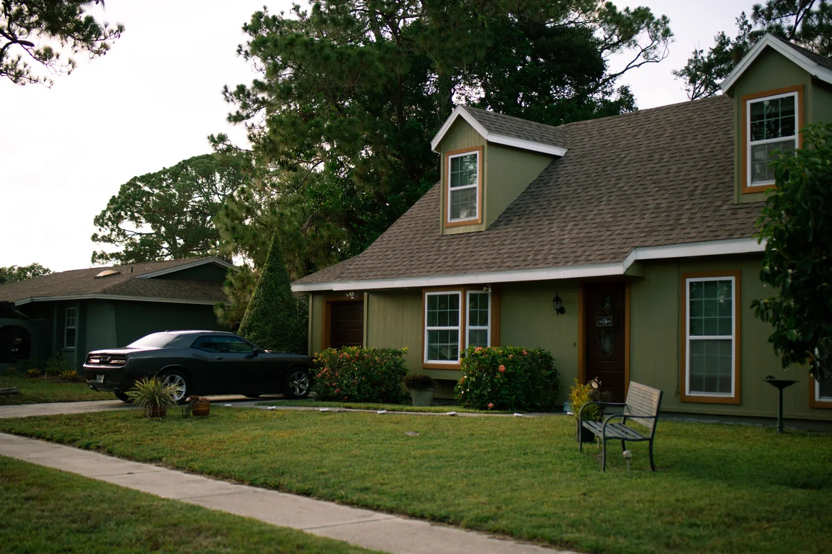Two-story home with dormer windows, contrasting siding, and a tree-lined lawn.