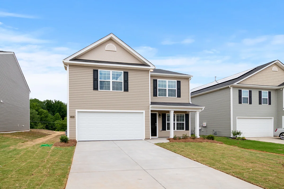 Light-colored two-story suburban home with a garage, front porch, and green lawn.