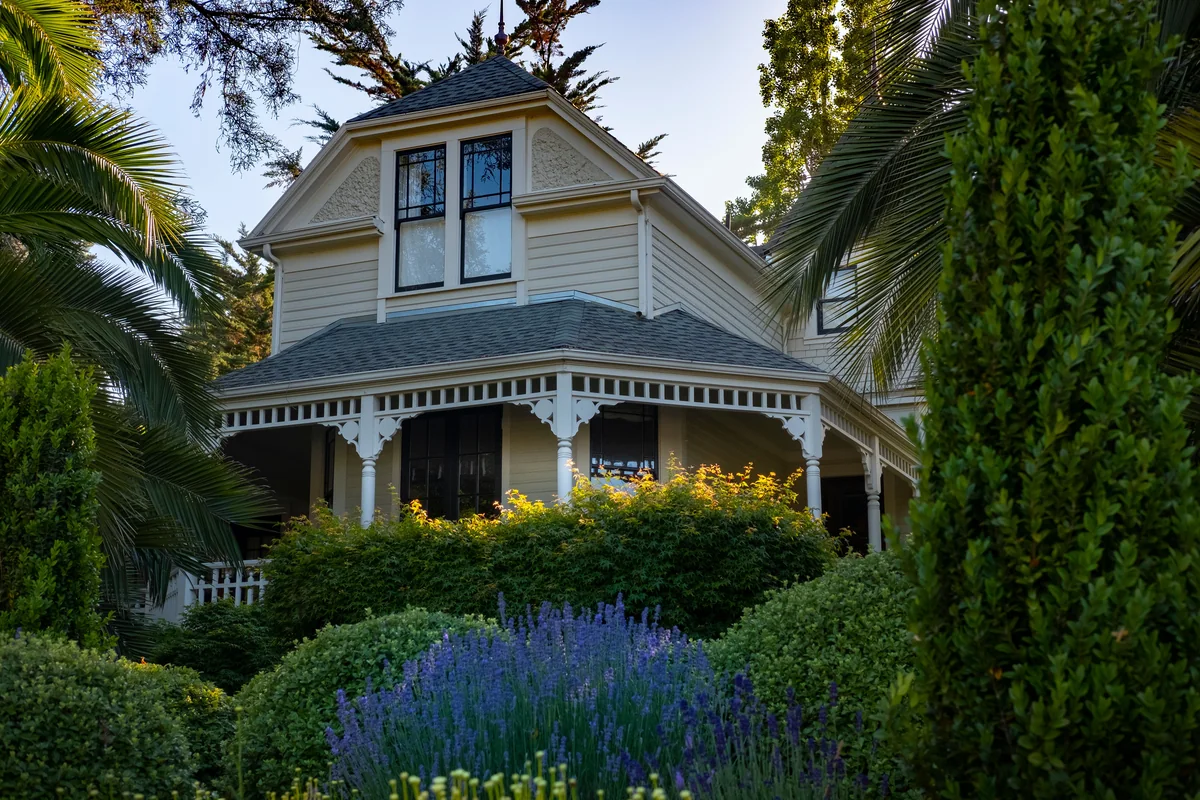 Traditional two-story house with a wraparound porch and flowering garden.