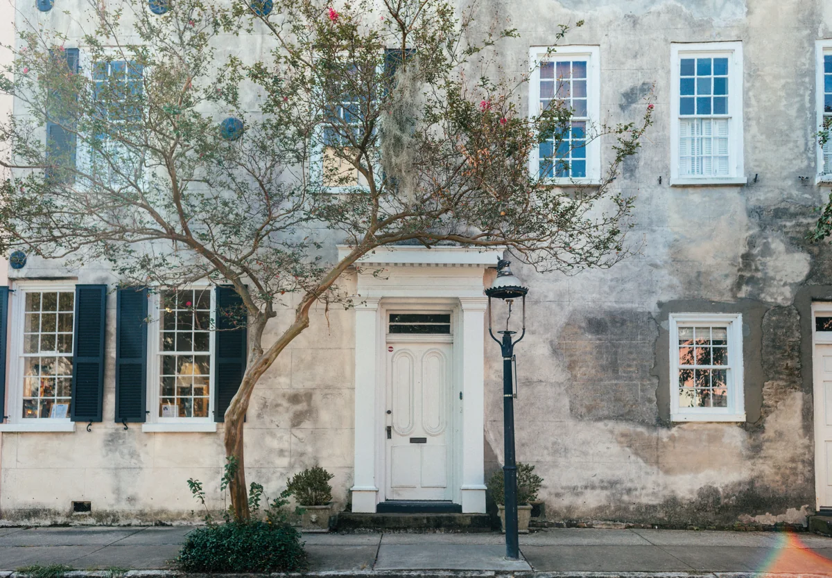 Historic house with a white door, shutters, and trees beside the facade.